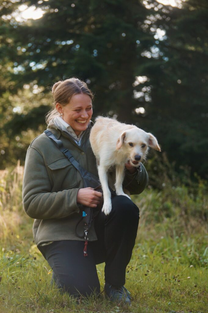 Hundetrainerin und Dogwalkerin mit ihrem Hund, der ihr auf den Schoß springt.